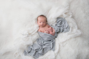 newborn baby boy sleeping on whte fur and fabrics wrapped in baby blue wrap