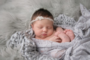 newborn baby girl sleeping on gray fur wrapped in lace