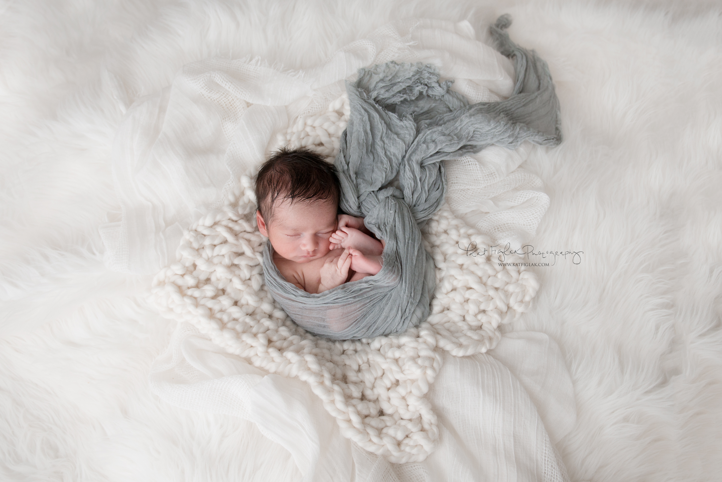 newborn baby boy on fur rug wrapped in gray wrap