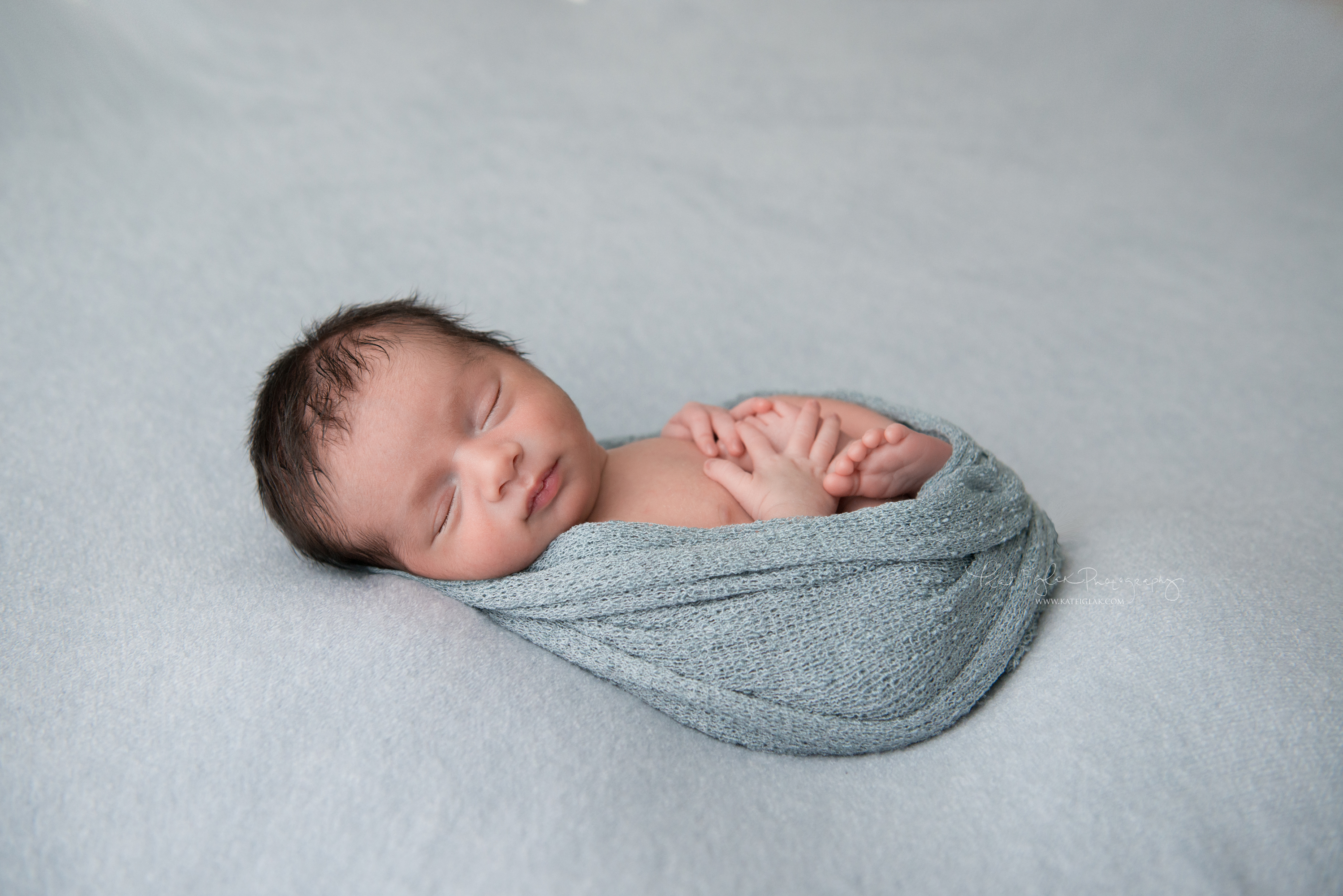 newborn baby boy sleeping on blue knit fabric wrapped in blue wrap