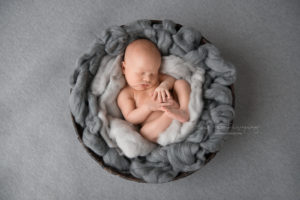 Newborn baby boy sleeping in basket with gray fluff