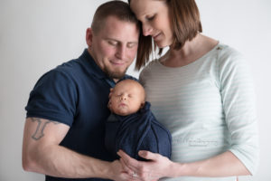 newborn baby boy wrapped in navy wrap being held by mom and dad