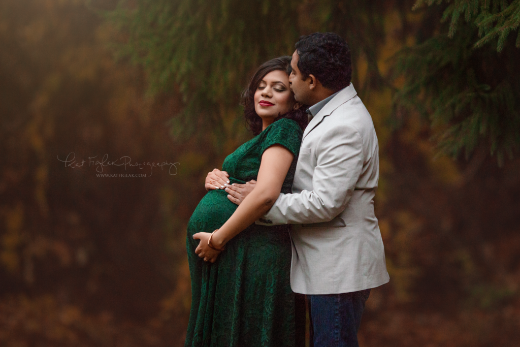 pregnant mom wearing an emerald gown while her husband kisses her head