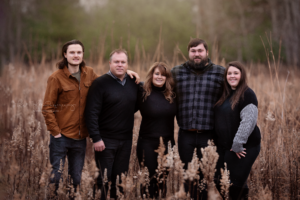 Family of 5 posed in tall grass in fall colors