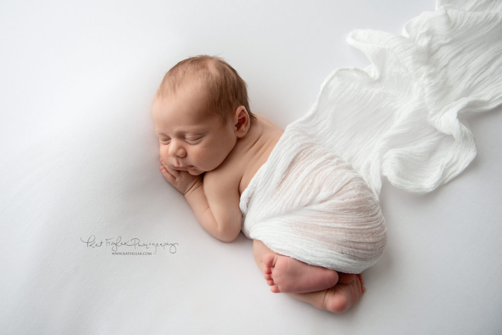 newborn baby boy sleeping on white blanket covered in white wrap