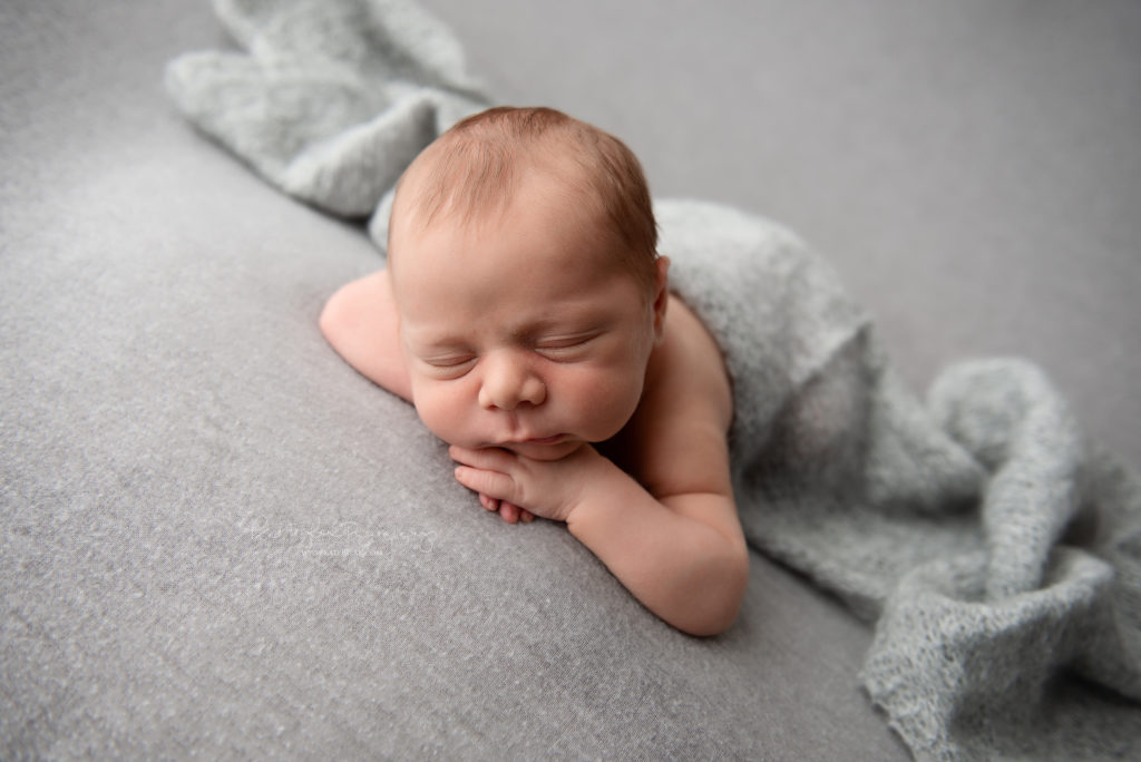newborn baby boy sleeping on a gray blanket covered in gray wrap