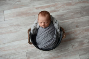 baby boy sleeping on a basket wrapped in a dark gray wrap