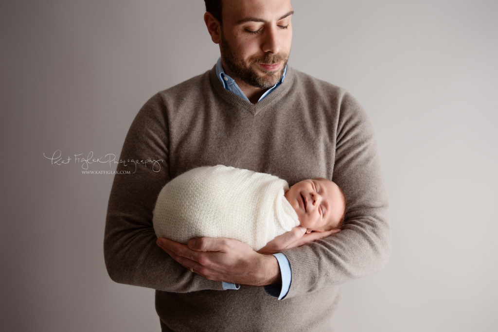 newborn baby boy smiling while being held in his dad's hands
