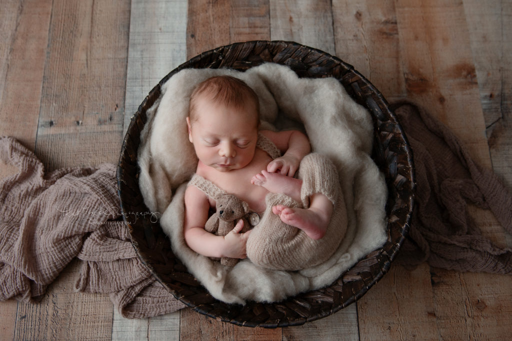 Newborn baby boy sleeping in basket while holding a little teddy bear