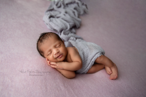 newborn baby girl sleeping on purple blanket smiling covered by purple wrap