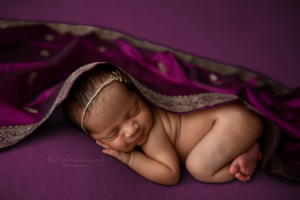 newborn baby girl sleeping on purple blanket covered in purple silk