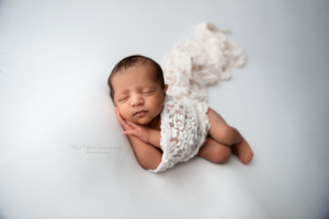 newborn baby girl laying on white blanket wrapped in white lace wrap