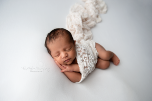 newborn baby girl sleeping on white blanket wrapped in lace wrap
