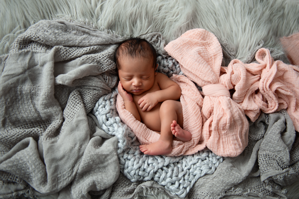 newborn baby girl sleeping in gray blankets wrapped in a pink wrap tied in a bow