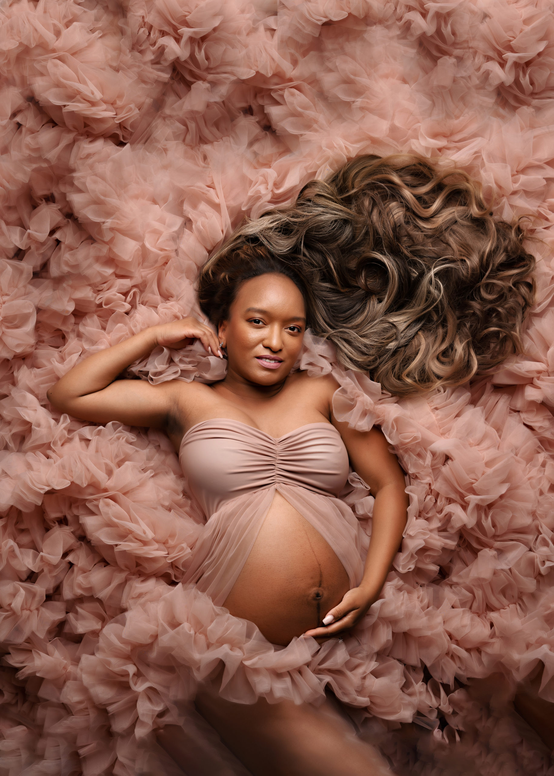 pregnant mom laying in pink tulle gown with dark hair flowing