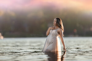 Mom wearing a beige beaded maternity gown standing in the lake
