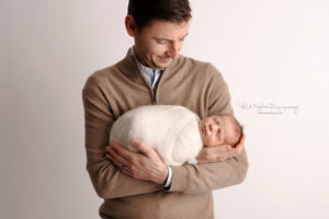 dad holding newborn baby wrapped in cream wrap