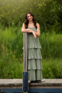 Oakland county senior girl wearing a sage green dress standing on a dock at Independence Oaks Park in Clarkston, MI