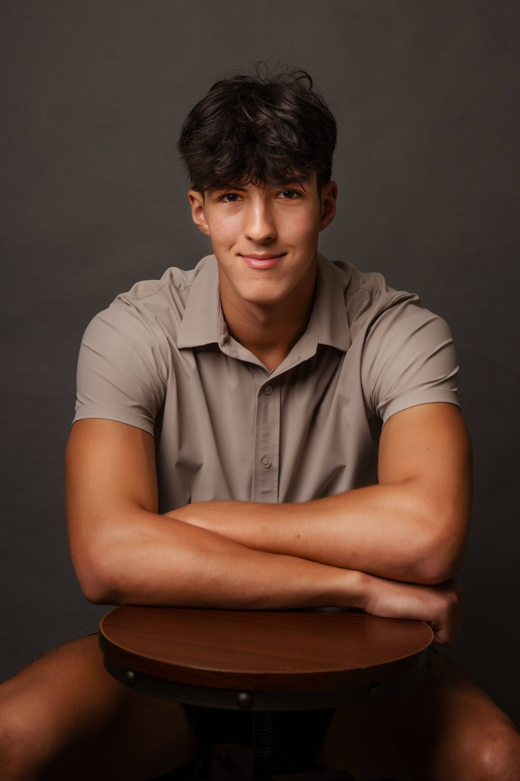 Flint Powers Catholic Senior boy wearing a tan shirt leaning on a stool with a dark backdrop
