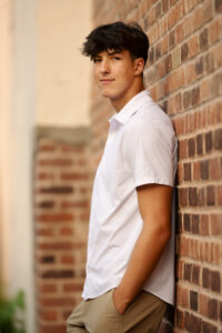 Flint Powers Catholic Senior boy wearing a white shirt leaning against a brick wall