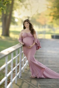 Pregnant woman standing on the boardwalk in Metro Park in Harrison Township, Michigan wearing a blush fitted gown holding her pregnant belly.