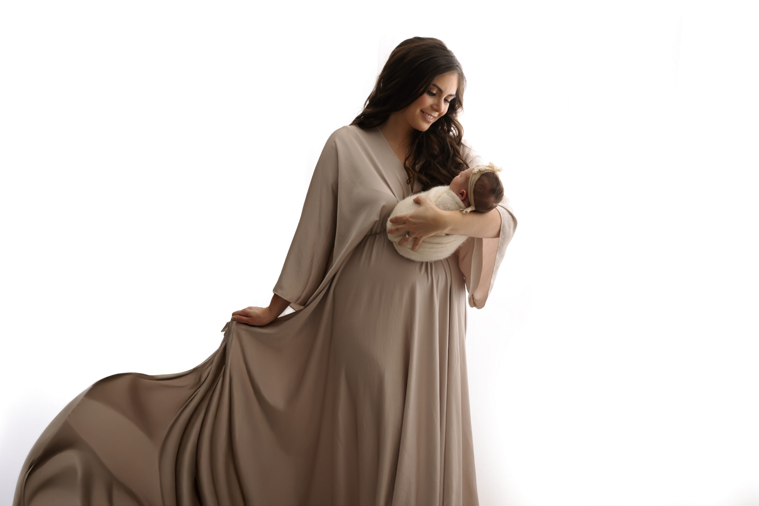 Mother wearing a flowy satin dress holding her newborn baby girl