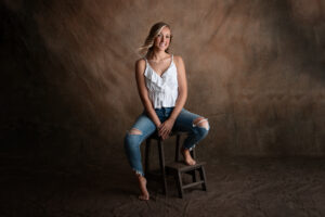 senior girl wearing a white tip and jeans sitting on a stool